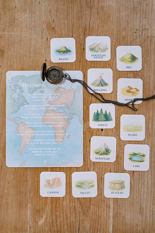 One large card with several smaller cards laying on a wooden table with a necklace compass laying across.